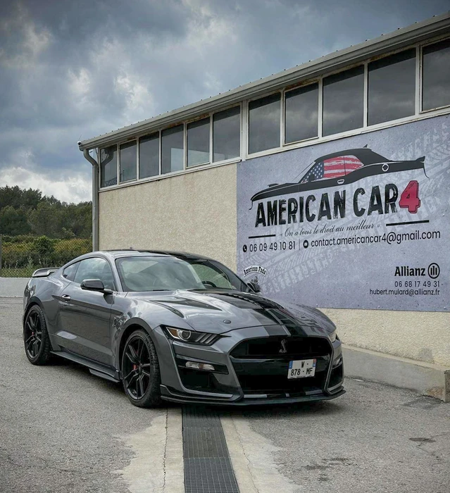 Extérieur d'un garage automobile spécialisé avec Ford Mustang Shelby GT500 grise à bandes noires garée devant