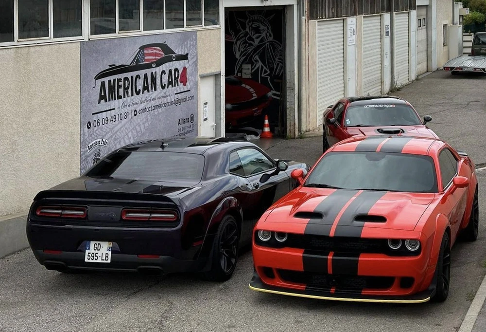 Extérieur d'un garage automobile spécialisé avec deux Dodge Challenger stationnées devant l'enseigne "American Car"