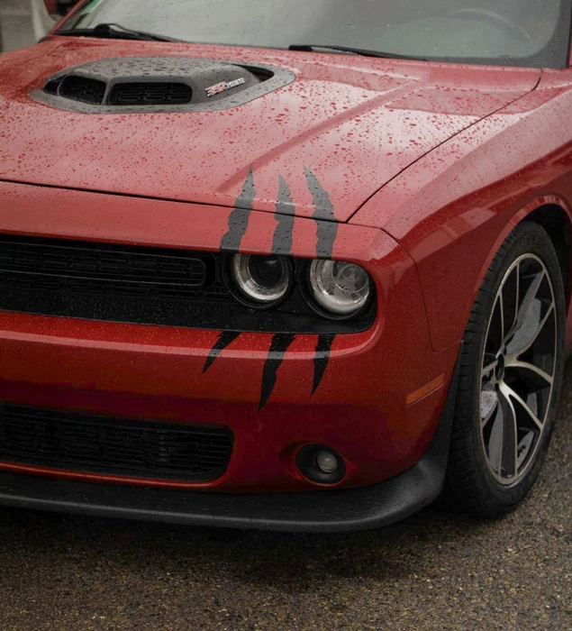 Extérieur, véhicule sportif rouge avec rayures noires garée sur asphalte mouillé, gouttelettes d'eau visibles sur carrosserie