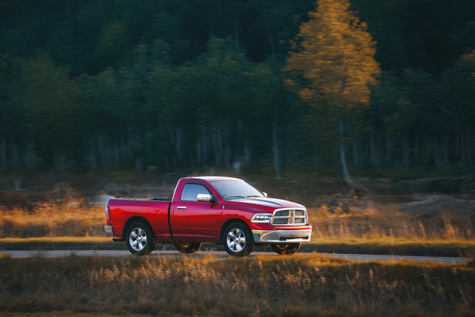 Homme d'affaires en costume sombre et cravate bleue consultant des documents sur presse-papiers, debout devant véhicule berline argentée dans environnement urbain extérieur